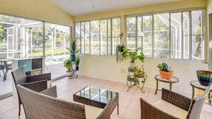 A sunlit room with wicker furniture, large windows, and potted plants.