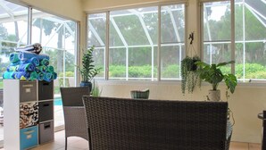 A room with large windows, wicker furniture, and a storage unit with folded towels.