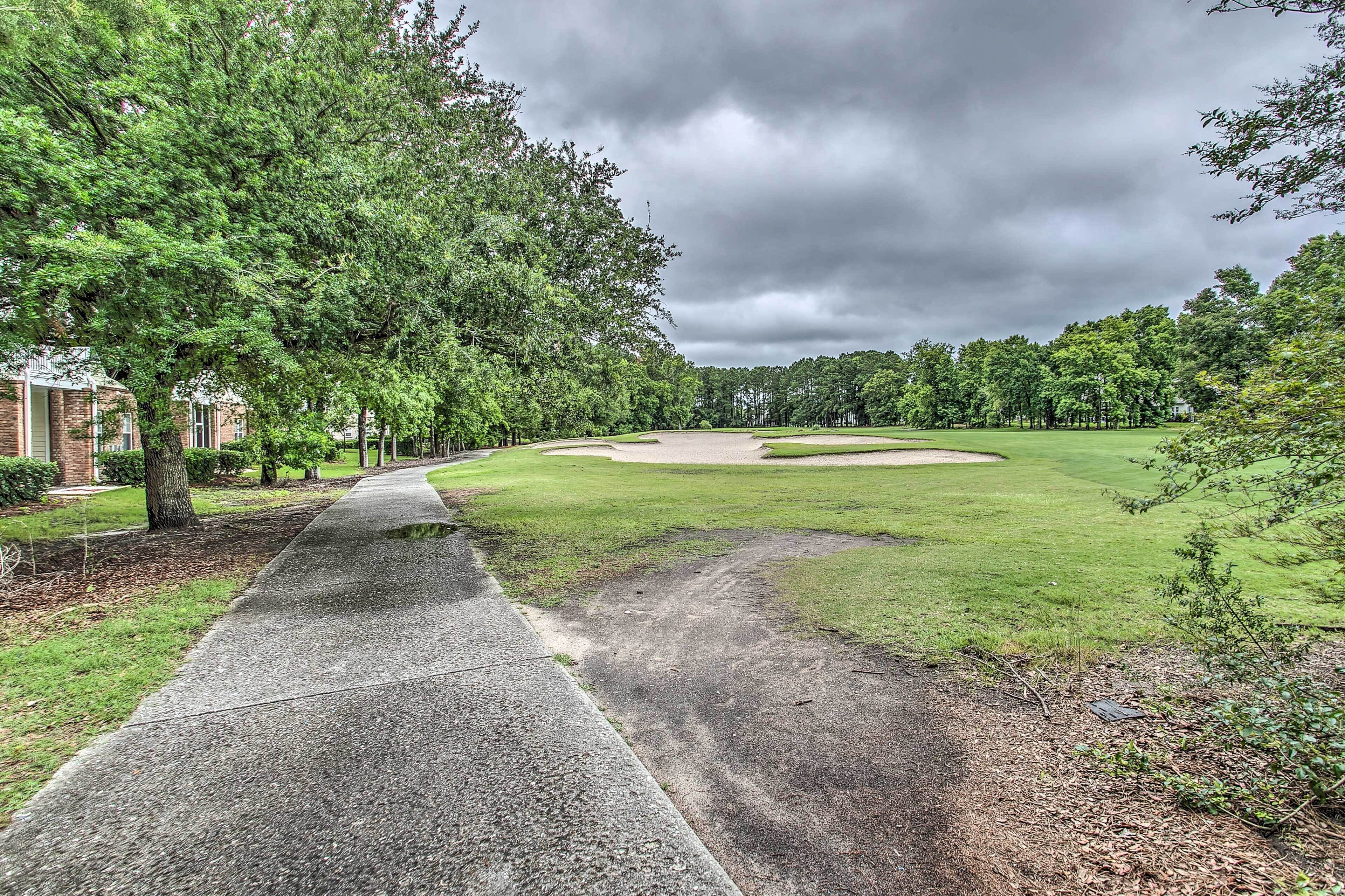 A pathway leading to a golf course with a building on the left.