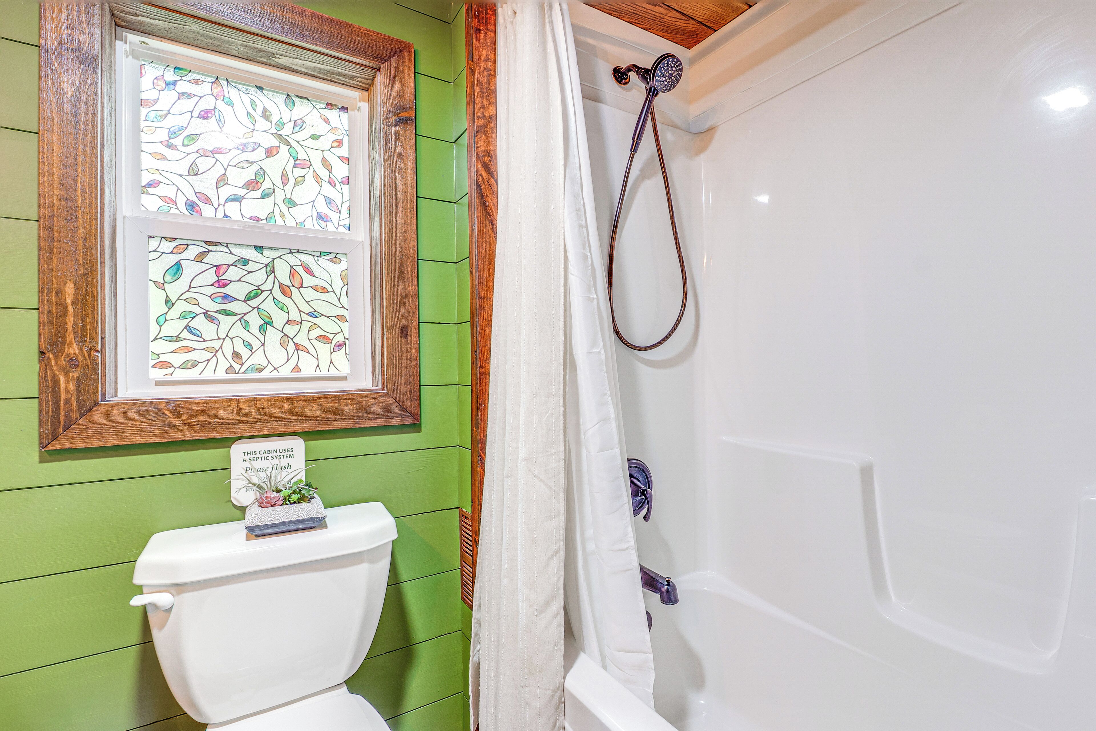 Ein Badezimmer mit grüner Wand, einer weißen Toilette, einer Duschkabine mit Vorhang und einem Buntglasfenster.
