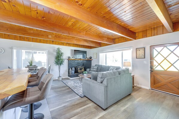 A spacious living area with a wooden ceiling, a fireplace, a sofa, and a dining table with chairs. - 2 Mi to Trails: Modern Mountain Condo in Big Bear (Big Bear City)