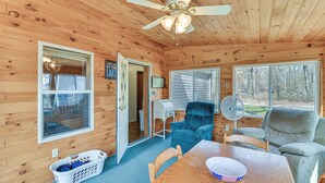 A wooden cabin interior with a dining table, two chairs, a ceiling fan, and large windows offering a view of the outdoors. - Waterfront Home w/ Boat Slips in Northern Michigan (Gladwin)
