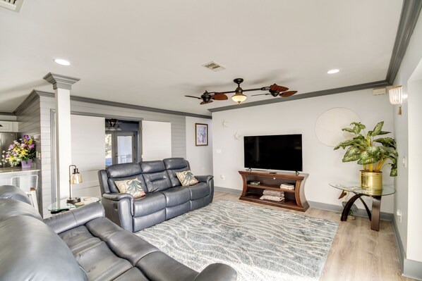 A modern living room with a leather sofa, a flat-screen TV, and a ceiling fan. - Front Row Beachfront Long Beach Getaway (Long Beach)