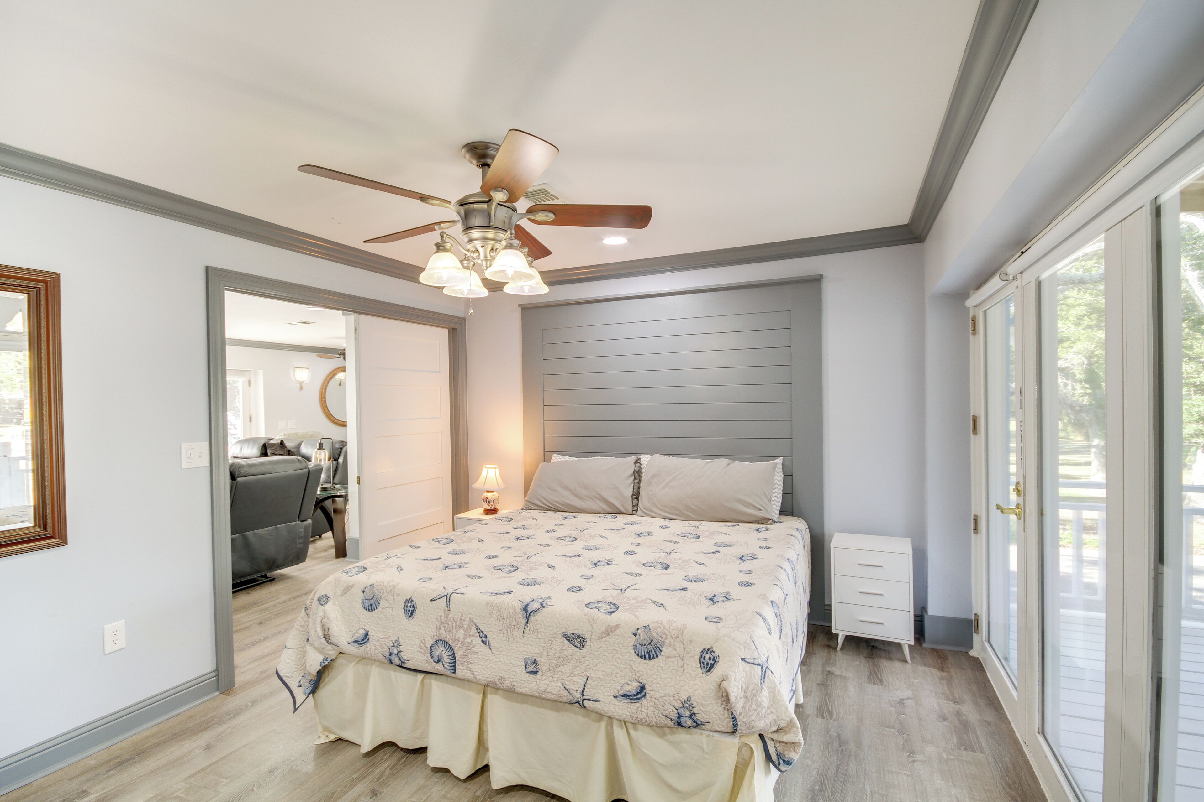 A bedroom with a bed, a ceiling fan, a nightstand, a dresser, and a sliding glass door to the outside.