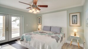 A bedroom with a bed, a ceiling fan, a nightstand with a lamp, and a door leading to a balcony. - Front Row Beachfront Long Beach Getaway (Long Beach)
