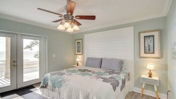 A bedroom with a bed, a ceiling fan, a nightstand with a lamp, and a door leading to a balcony.