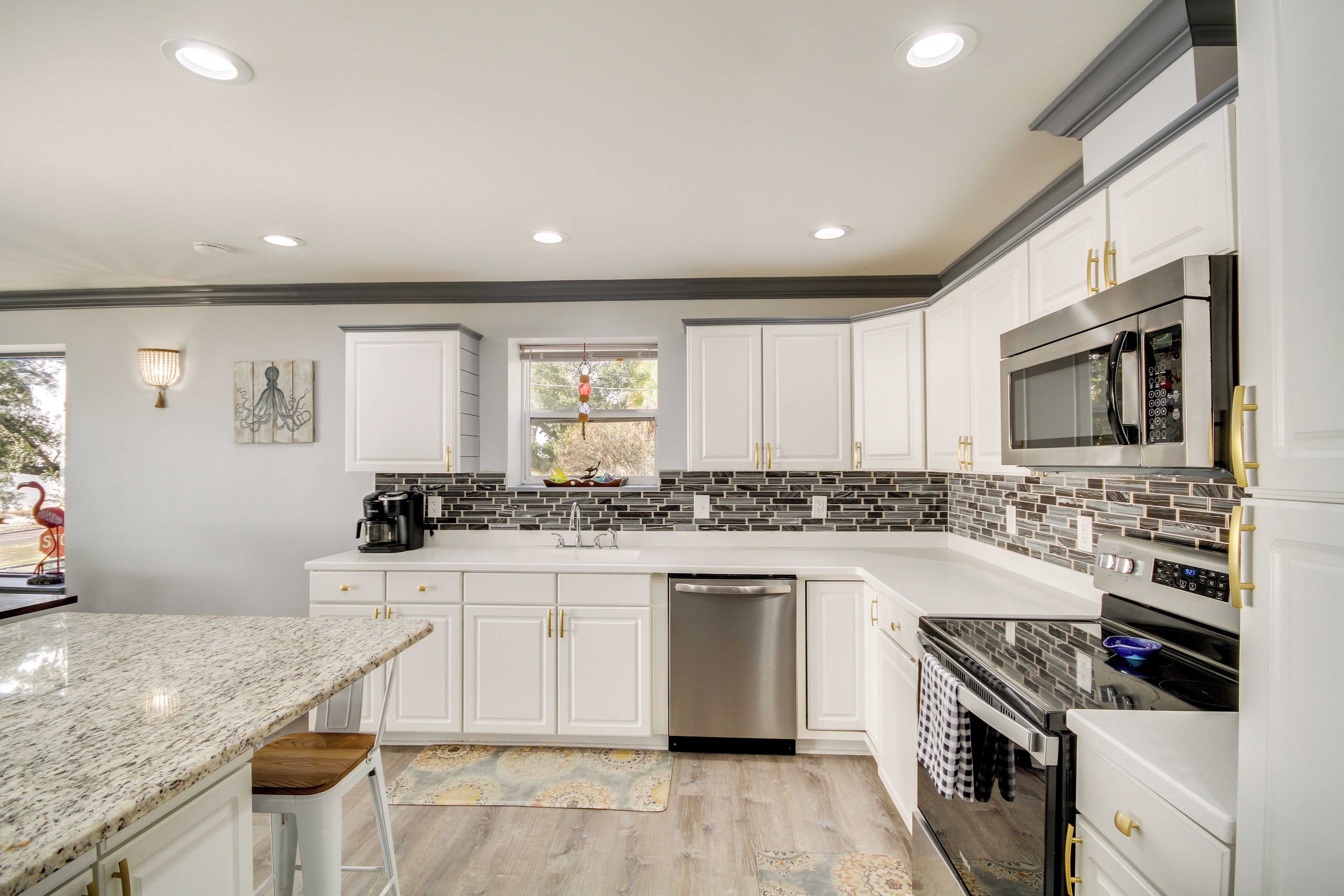 A modern kitchen with white cabinets, a granite countertop, stainless steel appliances, and a backsplash with gray and black tiles.