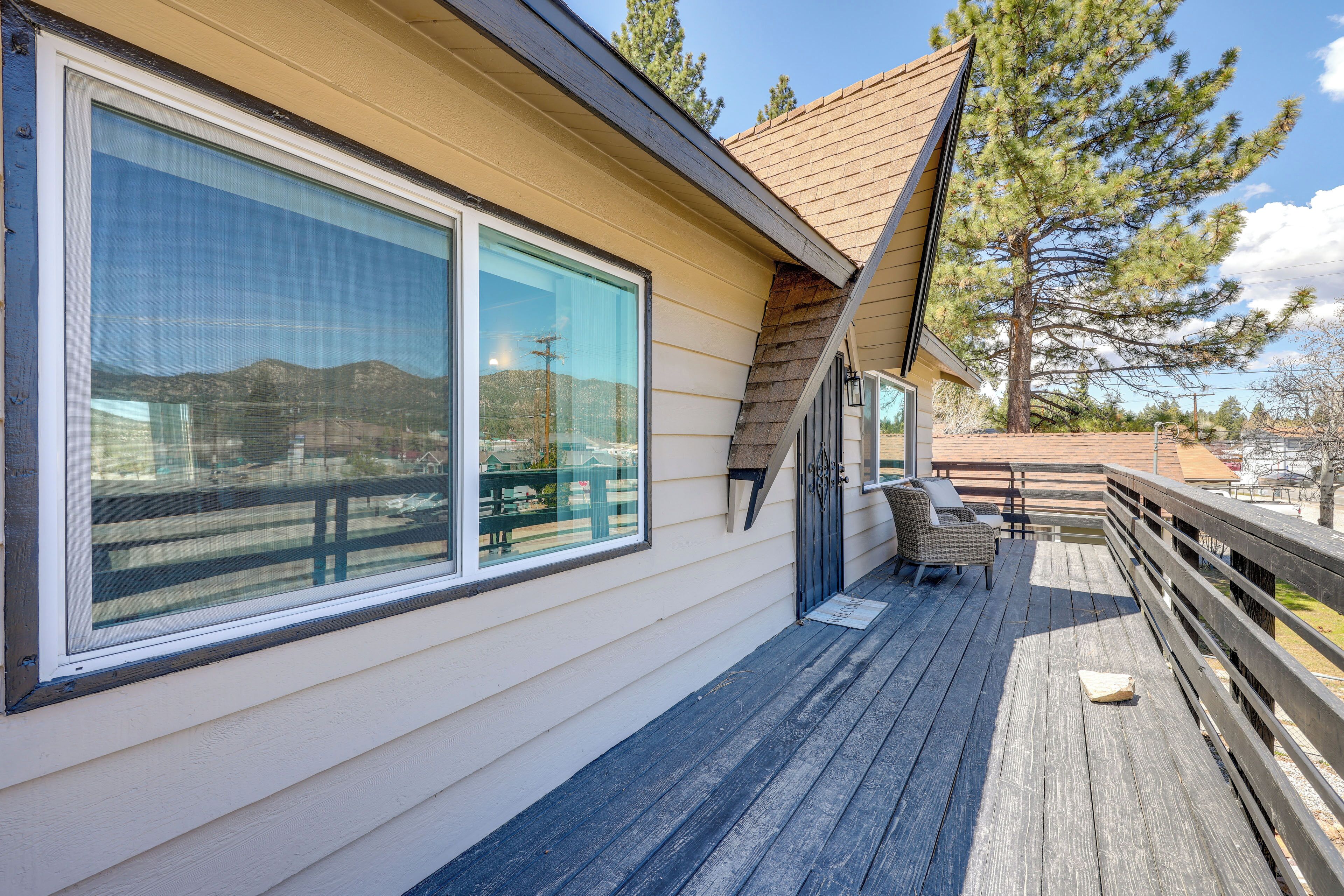 A wooden deck with a railing, a large sliding glass door, and a small outdoor seating area with a bench and table.
