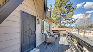 A wooden deck with wicker furniture and a welcome mat, overlooking a street and trees. - Close to Skiing & Lake: Big Bear Mountain Getaway (Big Bear City)