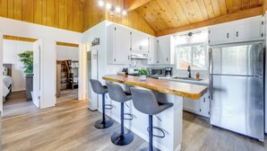 A modern kitchen with wooden ceiling beams, a central island with bar stools, stainless steel appliances, and white cabinetry. - Close to Skiing & Lake: Big Bear Mountain Getaway (Big Bear City)