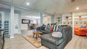 A modern living room with a sectional sofa, a coffee table, and a dining area in the background. - Spacious Yard & Bbq: Chic Escape in Lawrenceville! (Lawrenceville)