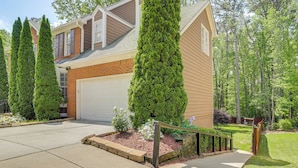 A two-story house with a garage, a well-maintained lawn, and tall evergreen trees. - Spacious Yard & Bbq: Chic Escape in Lawrenceville! (Lawrenceville)