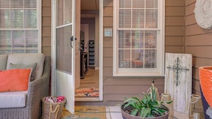 A cozy entryway with a wicker sofa, a potted plant, and a wooden door with a cross decoration. - Spacious Yard & Bbq: Chic Escape in Lawrenceville! (Lawrenceville)