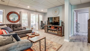 A spacious living room with a large sofa, a coffee table, and a television. There is a fireplace and a large mirror on the wall. - Spacious Yard & Bbq: Chic Escape in Lawrenceville! (Lawrenceville)