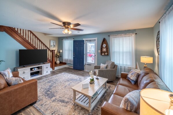 A living room with a TV, sofa, coffee table, and a staircase. - Family-Friendly 4Br Near Beach, Smart Tv Fun (Wildwood)