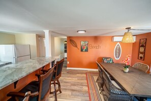 Une cuisine moderne dotée d’un plan de travail en marbre, de chaises en bois et d’un coin repas avec une longue table et des chaises en osier.