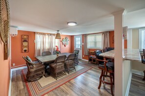 A dining area with a large table and wicker chairs, a small side table, and a window with blinds. - Family-Friendly 4Br Near Beach, Smart Tv Fun (Wildwood)