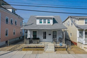 A two-story residential building with a grey roof, white trim, and a front porch with a small garden area. - Family-Friendly 4Br Near Beach, Smart Tv Fun (Wildwood)
