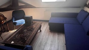 A loft-style room with a skylight, a blue sofa, a dark wooden coffee table, and a vintage globe on a wooden chair. - Country apartment (Moulins)