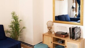 Een woonkamer met een blauwe bank, een witte salontafel, een blauwgroen voetenbankje, een houten kast met spiegel en een bamboe plant.