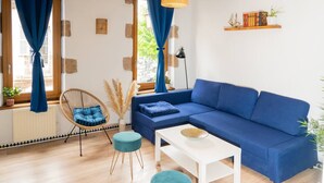 Een moderne woonkamer met een blauwe bank, een rieten stoel, een witte salontafel en een kleine ronde tafel.