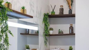 Casa de banho com duas pias, um espelho e prateleiras com plantas e objetos decorativos.