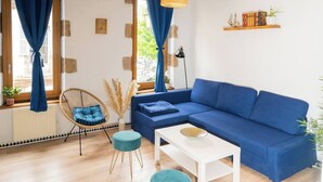 Uma sala de estar moderna com um sofá azul, uma mesa de centro branca e uma cadeira de vime.