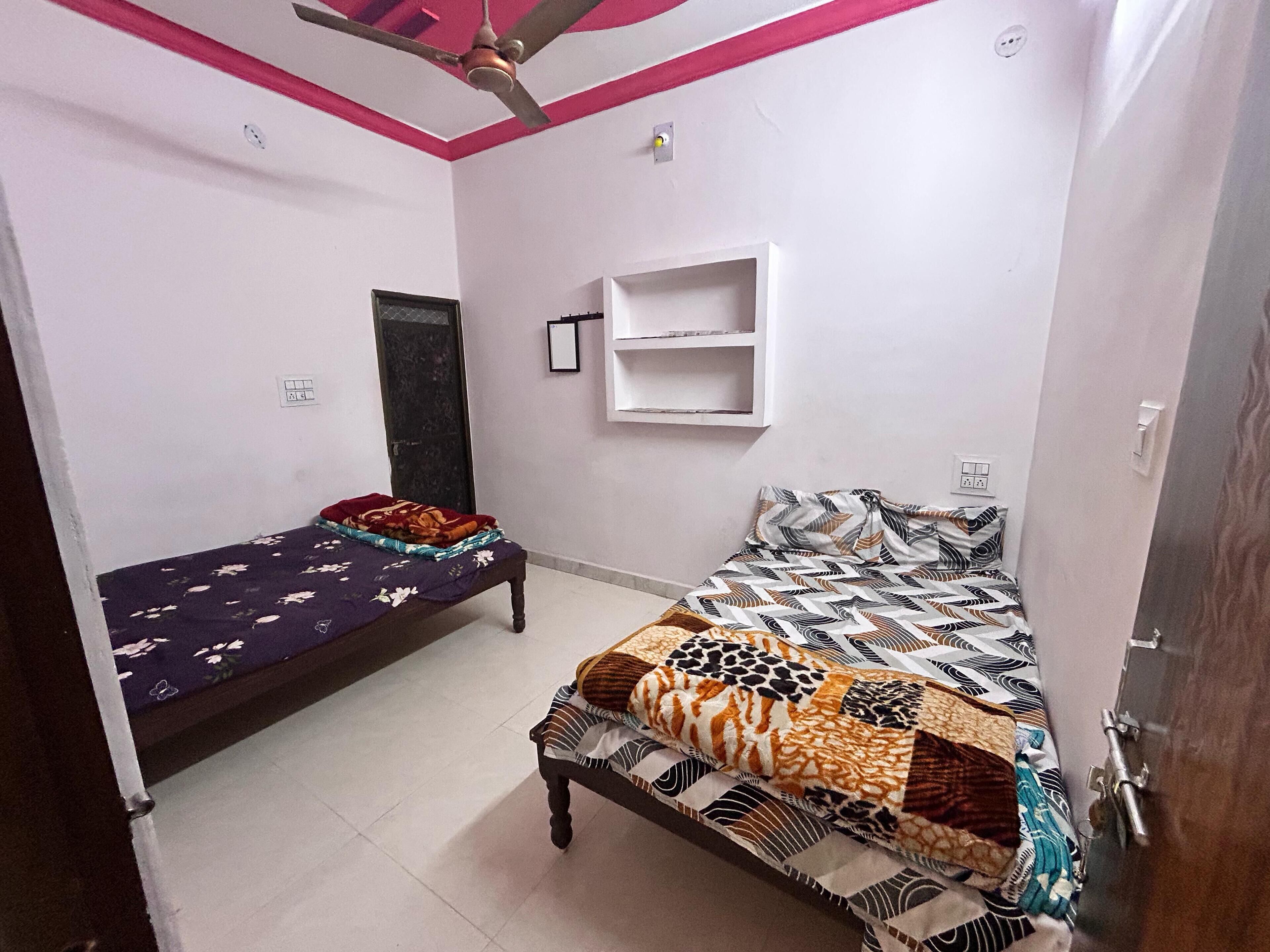 A bedroom with two beds, a ceiling fan, a small shelf, and a door.