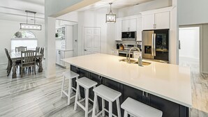 A modern kitchen with a large island, white cabinetry, stainless steel appliances, and a dining area with a wooden table and chairs.