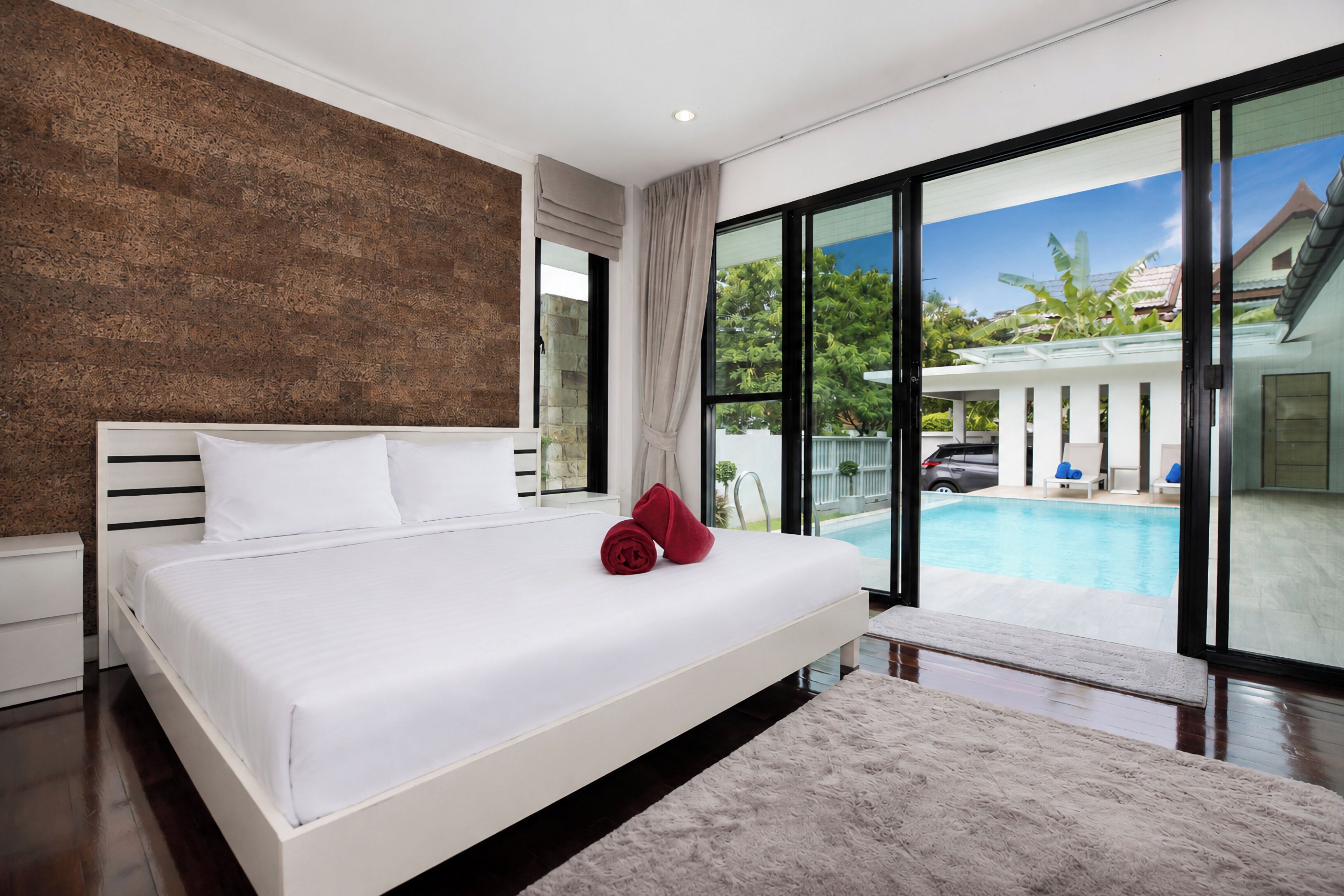 Ein modernes Schlafzimmer mit einem großen Bett, Blick auf einen Pool und einer Steinwand.