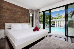 A modern bedroom with a large bed, a view of a swimming pool, and a stone wall. - Designer 3BR Villa Silver Pool in Kamala (Kamala)