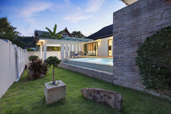 A modern house with a swimming pool, stone walls, and a well-maintained lawn.