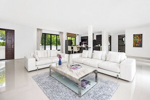 A modern living room with a white sectional sofa, a glass coffee table, and a view of the kitchen through an open door. - Designer 3BR Villa Silver Pool in Kamala (Kamala)