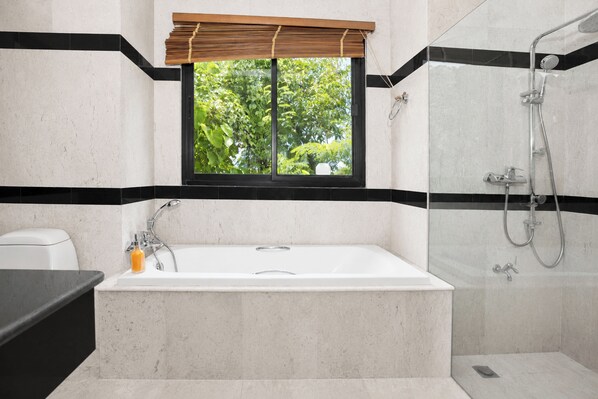 A bathroom with a bathtub, a shower, and a window with a view of greenery.