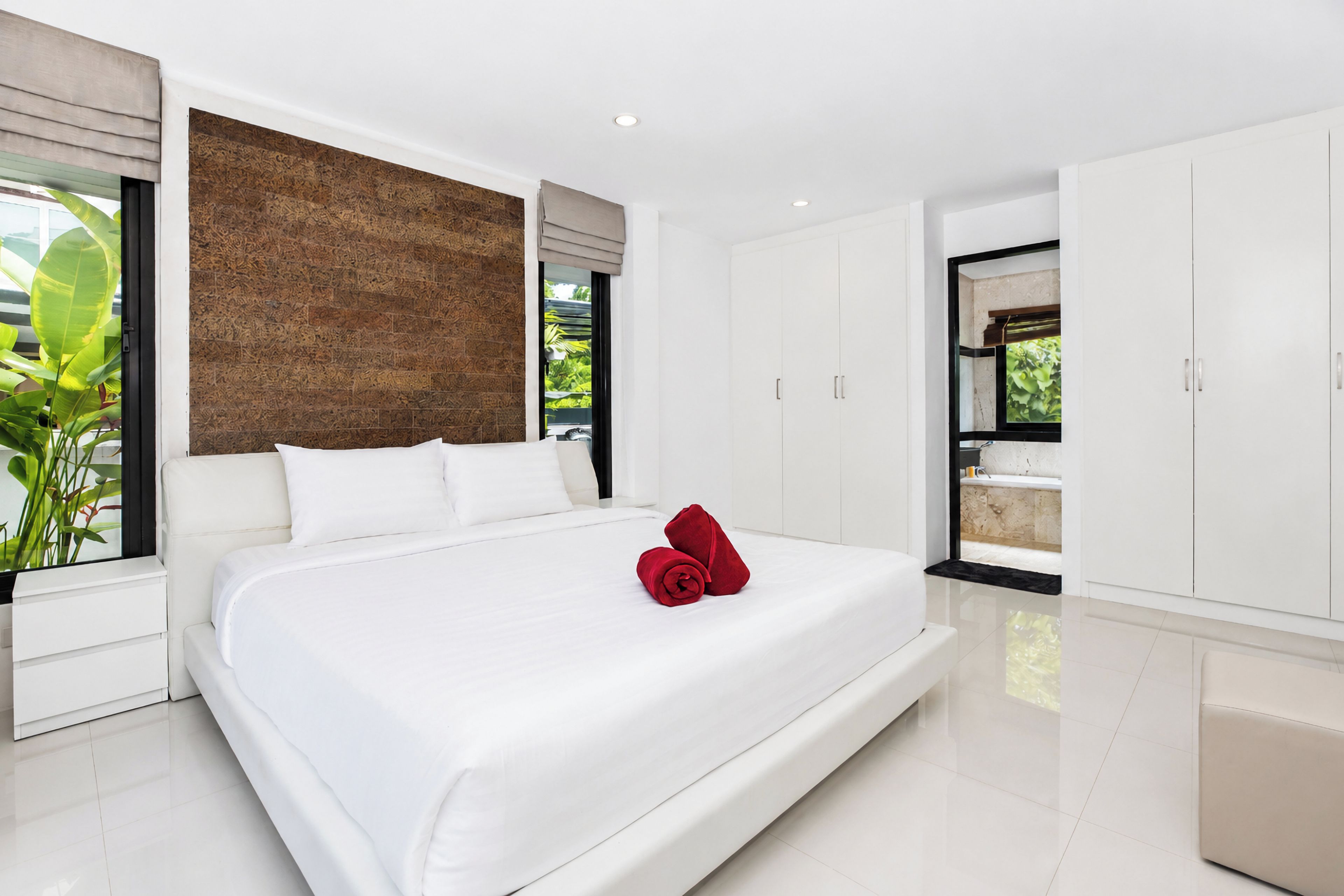 Un dormitorio moderno con una cama grande, paredes blancas, un panel de madera decorativo y vistas a zonas verdes.