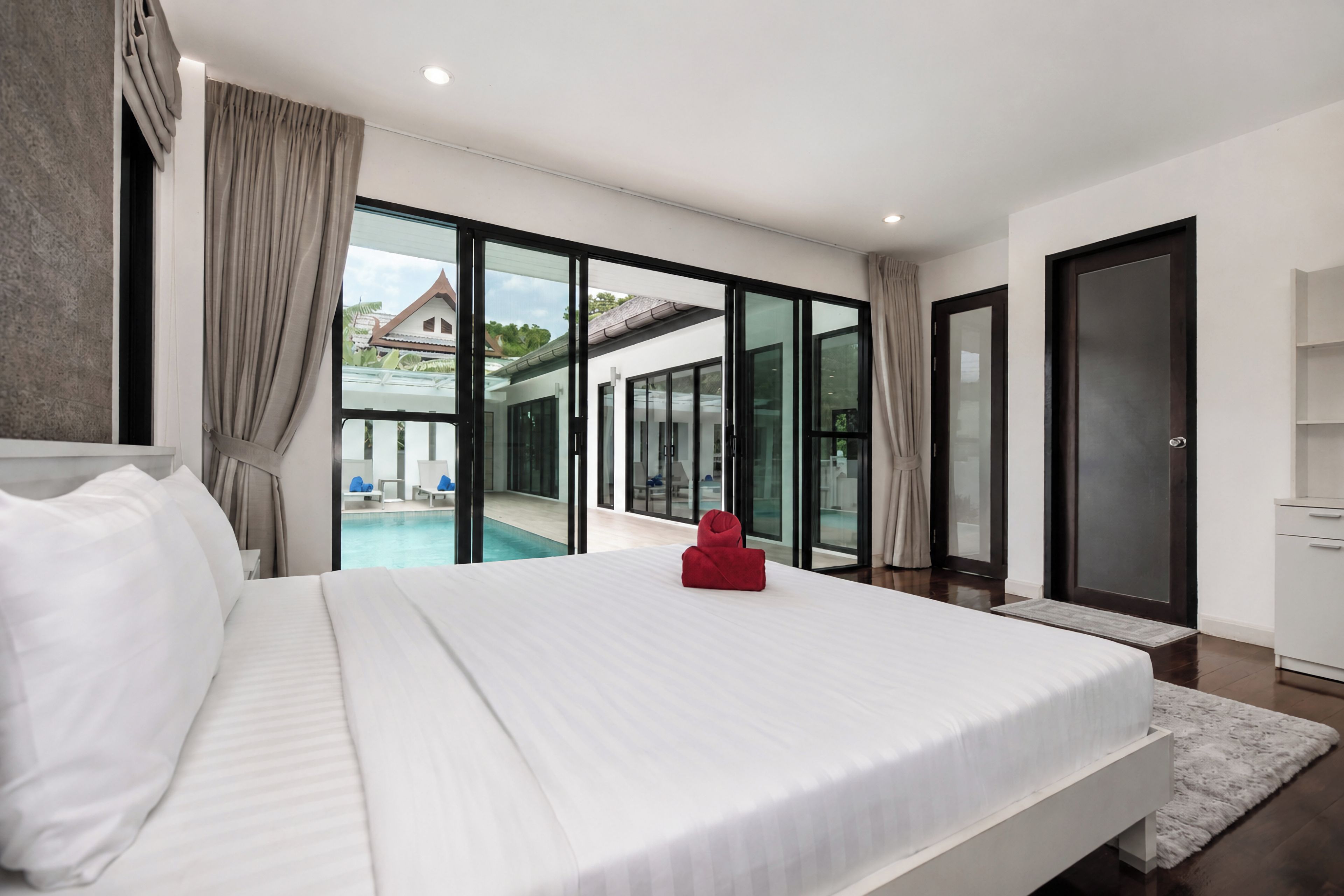 Habitación de hotel moderna con una cama grande, vista a una piscina y puerta corrediza de vidrio que da a un balcón.