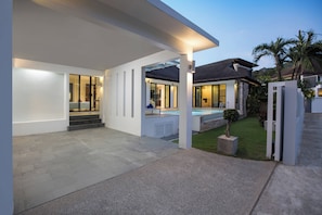A modern house with a covered patio, a swimming pool, and a well-maintained lawn.
