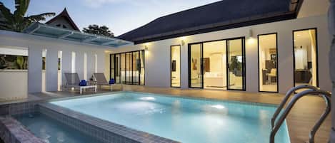 A modern pool area with clear glass walls, lounge chairs, and a well-lit interior.