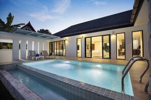 A modern pool area with clear glass walls, lounge chairs, and a well-lit interior.