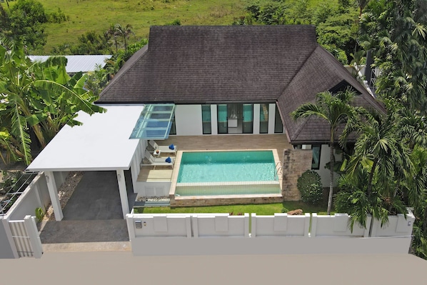 A modern house with a swimming pool, a covered patio, and a view of a lush green landscape.