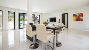 A modern dining area with a black table, white chairs, and a large window. - Designer 3BR Villa Silver Pool in Kamala (Kamala)