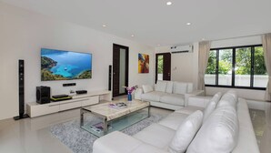 A modern living room with a large flat-screen TV, white leather sofa, and a glass coffee table. - Designer 3BR Villa Silver Pool in Kamala (Kamala)