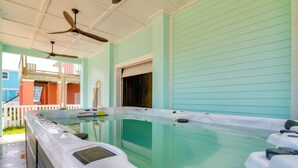 A hot tub area with a ceiling fan, a window, and a view of a colorful building outside. - Swim Spa, Game Room: New Build Navarre Beach House (Navarre)