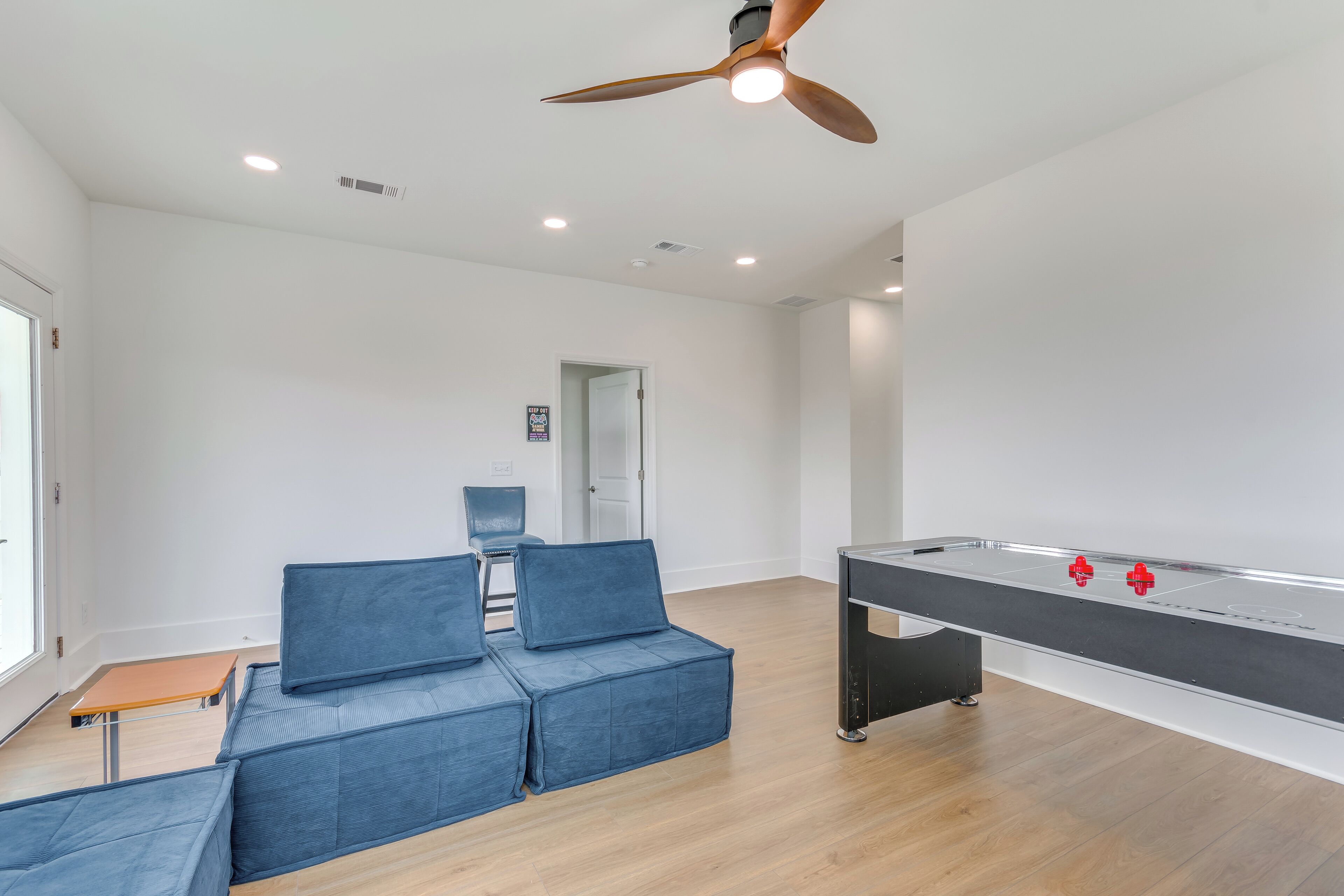 A spacious room with a foosball table, a ceiling fan, and a seating area with blue cushions.