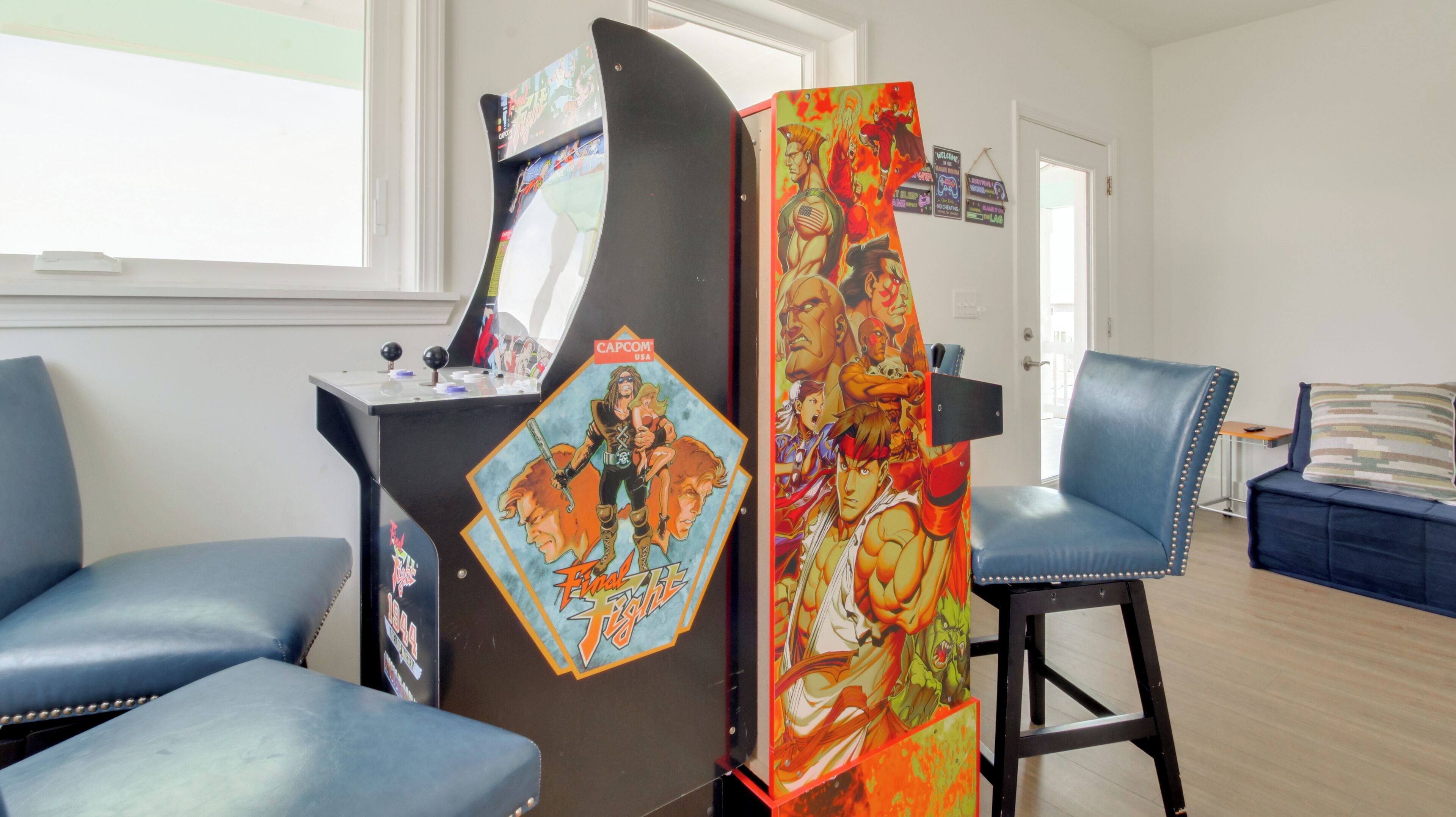 A room with a gaming arcade, blue chairs, and a door with colorful artwork.
