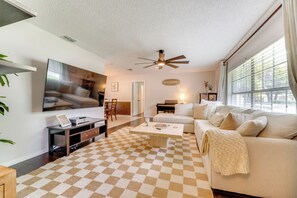 A living room with a checkered floor, a ceiling fan, a flat-screen TV, a sofa, a coffee table, and a window with curtains. - Private Outdoor Oasis w/ Pool: Home in Longwood! (Longwood)