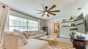 Ein Wohnzimmer mit einem beigefarbenen Ecksofa, einem Couchtisch, einem Deckenventilator und einem karierten Teppich.