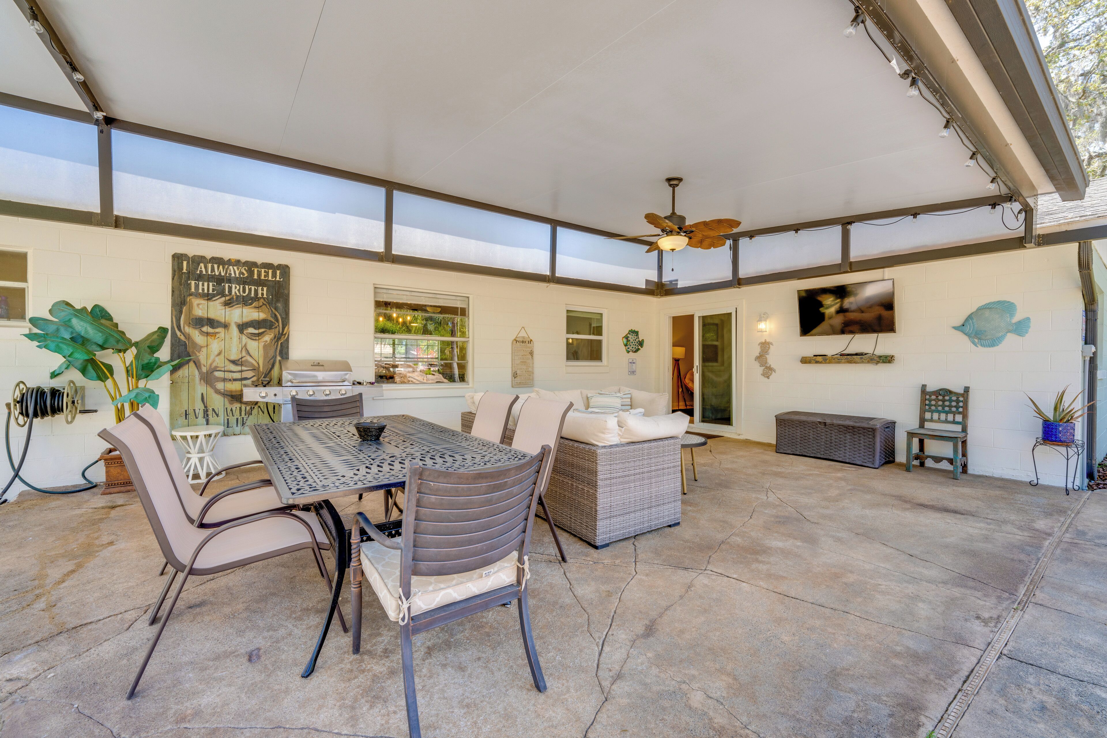 An outdoor patio area with a table and chairs, a ceiling fan, and a wall-mounted TV.