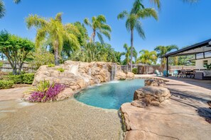 A pool with a waterfall, surrounded by rocks and palm trees. - Private Outdoor Oasis w/ Pool: Home in Longwood! (Longwood)