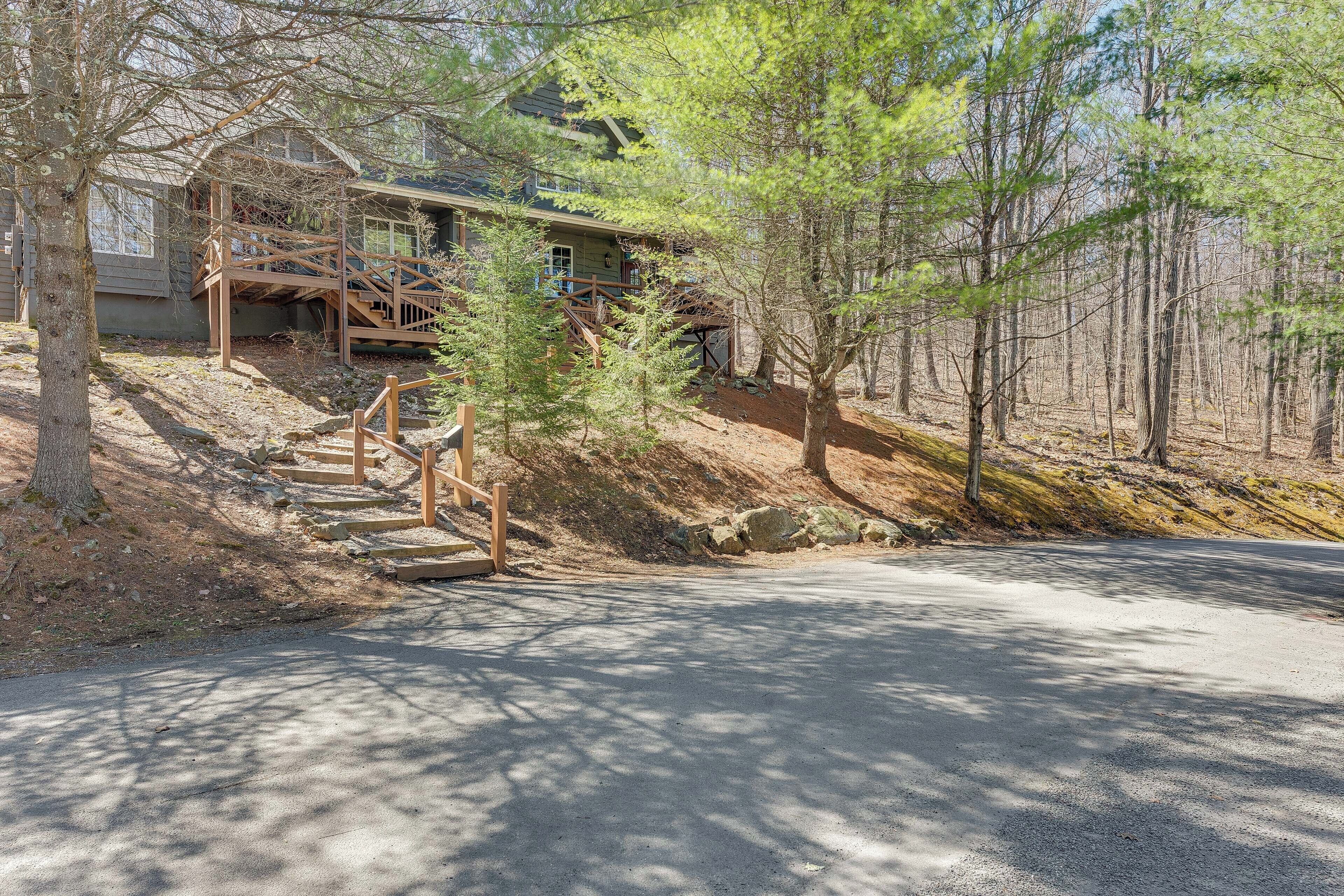 A cabin with a wooden staircase leading to a porch, surrounded by trees and a dirt path.